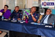 NRA Commissioner General Calls for Stronger Revenue Mobilisation as Familiarization Tour Begins Panel of four people seated at a conference table; two in uniform, one woman in purple, one man in a suit, purple vase of flowers center stage; NRA logo in background.