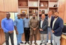 BB Energy LPG Project Sparks Calls to Protect Sierra Leonean Businesses from Market Displacement Seven men in smart-casual attire pose in a wood-paneled office, with shelves of plaques and trophies behind them.