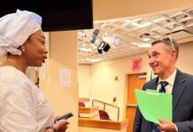 ICPNC Executive Secretary Takes Sierra Leone’s Peace Model to UNGA81 Global Stage Two professionals chat in a hallway: a woman in white traditional attire holding a phone, facing a man in a suit with a bright green folder.