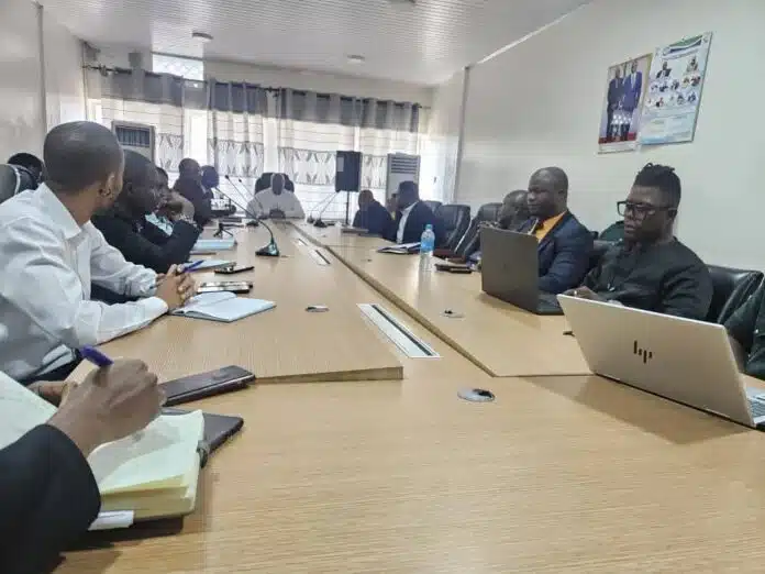 A group of professionals seated around a long conference table, some with laptops and notebooks, in a meeting room.