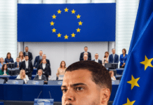 European Parliament Resolution Imposes No Sanctions on Sierra Leone, Puts Bolle Jos Case in Wider Spotlight Man in a white shirt in front of a European Parliament setting with EU flag imagery and a circular group of stars behind him.