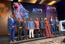 Umaru Napoleon Koroma Urges Africa to End Raw Mineral Exports Group of dignitaries in formal attire posing on a stage at an AOW Energy event, with a large lion mural and Africa map backdrop.