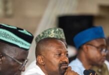 VP Juldeh Jalloh Expands Nationwide Decentralization Drive to Makeni and Port Loko Man in white traditional attire rests his chin on his hand at a panel, microphones in front of him.