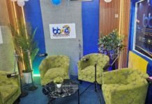 BBN Media Launches Podcast and Multimedia Studio to Expand Digital Storytelling Radio studio interview set with four green patterned chairs around a black marble coffee table, microphones on stands, plants, and branding on blue/gray walls.