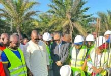 Timothy Kabba Secures Chinese Funding for ETU’s Landmark Postgraduate Complex Group of construction workers and officials in safety vests and hard hats observe as a crew member places a concrete block at a construction site, with palm trees in the background.