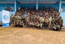 CHRDI Trains 128 RSLAF Personnel on Humanitarian Law Ahead of UN Peacekeeping Deployment Group of soldiers in camouflage posing for a group photo outside a blue building, with a CHRD banner on the left.
