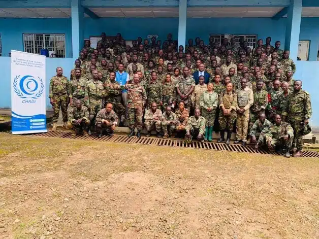 Group of soldiers in camouflage posing for a group photo outside a blue building, with a CHRD banner on the left.