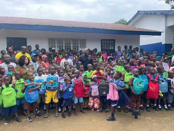A large group of schoolchildren with colorful backpacks standing outside a classroom building.