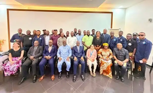 Group of about 30 professionals posing for a group photo in a conference room; front row seated in suits and dresses, back row standing in smart casual attire.