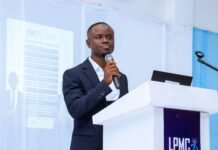 PAN Kick-Starts 2026 Leadership and Public Speaking Masterclass Man in a dark suit speaking into a handheld microphone at a white podium with a laptop, LPMC logo on the front panel.