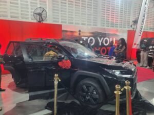 Black Toyota Land Cruiser on display at an auto show with doors open and a red backdrop.
