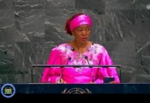 First Lady Fatima Bio Makes History as UN Adopts Landmark Resolution to End Child Marriage Female speaker in a bright pink traditional outfit and headwrap delivering a speech at the United Nations podium with microphones visible.