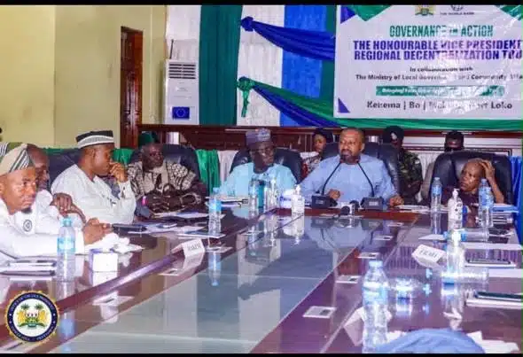Panel of officials seated around a conference table during a regional development forum, with a banner in the background.
