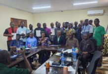 Lands Ministry Licenses 18 Surveyors, Calls for Professionalism and Integrity Group of about 24 people in a conference room, some holding documents, seated around a U-shaped table with water bottles on it.