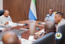 President Bio, VP Drive Preparations for Historic West Africa Integration & Investment Summit A formal government meeting with officials seated around a wooden conference table, microphones and documents in front of them, and a national flag in the background along with an official seal.