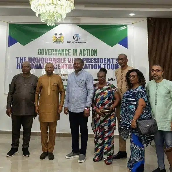 Seven people pose for a photo in a conference room in front of a banner that reads Governance in Action at an official event.