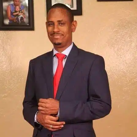 Man in a navy suit and red tie posing with hands clasped in front.