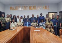 NCRA Marks International Identity Day with Registration Drive for 100 Inmates Group of uniformed officers and civilians posing for a photo in a conference room with a long wooden table and a wall sign reading MajGen. Sdt. Ngaujah Hall behind them.
