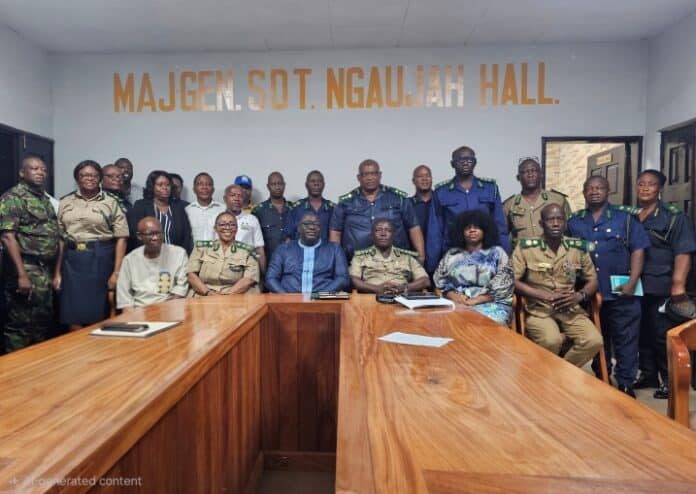Group of uniformed officers and civilians posing for a photo in a conference room with a long wooden table and a wall sign reading MajGen. Sdt. Ngaujah Hall behind them.