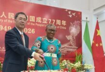 Chinese Embassy Celebrates 77th Anniversary, 55 Years of Diplomatic Ties with Sierra Leone Man and woman cut a large cake at a 77th anniversary celebration for the People's Republic of China, with Chinese flags in the background.