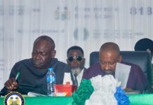 Finance Minister Outlines Fiscal Reforms as FY2027 Budget Process Begins Two men in a formal meeting sit at a green-draped table; one writes with a pen, the other reads a document, with an official seal visible on the left.