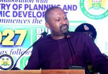 Vice President Calls for Growth-Focused FY2027 Budget as Sierra Leone Targets 500,000 Youth Jobs Man in a purple traditional outfit delivering a speech at a podium with two microphones, against a backdrop of banners and emblems.