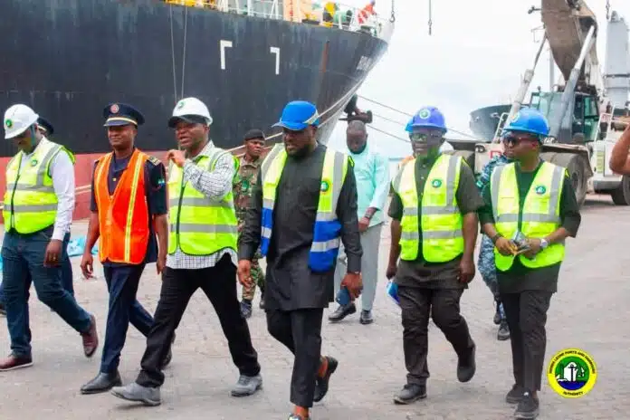 Group of port workers in high-visibility vests and hard hats walking along a dock with a large cargo ship in the background.
