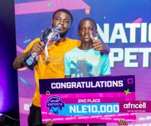 Two young men celebrate on stage; one holds a trophy and the other gives a thumbs up, standing behind a large banner that reads 'CONGRATULATIONS' and '2ND PLACE NLE 10,000' with a colorful event backdrop.