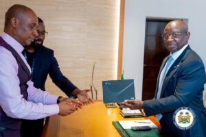 Two men in formal attire exchange a dark card across a polished desk during a formal meeting in a government office.
