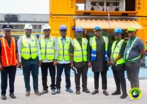 Team of construction workers in safety vests posing for a photo at a port or construction site with orange containers in the background.