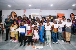 Group of smiling children and adults posing with certificates at an Orange Digital Center ceremony in a bright room.