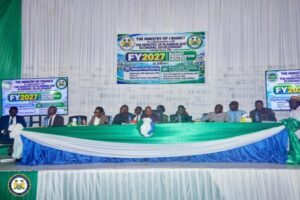 Panel of officials seated behind a long green-and-blue table on a stage, with FY2027 banners for a government budget planning event in the background