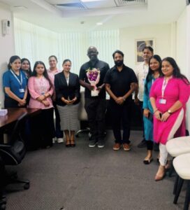 Group of ten colleagues standing in an office, one person in the center holding a bouquet of flowers.
