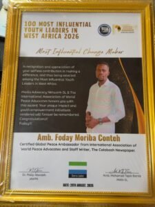 Framed award certificate titled '100 Most Influential Youth Leaders in West Africa 2026' with a photo of a man in a white striped shirt; date August 29, 2026, signatures present in bottom area.