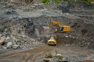 Yellow excavator loads a bucket of rock into a yellow dump truck in a rocky quarry pit