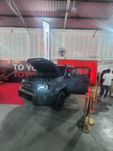Dark Toyota pickup on display with hood up and passenger door open at an indoor showroom