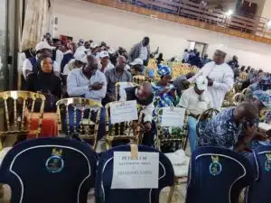 Conference hall filled with attendees seated in gold chairs; signs on chairs read Petroleum, Telecommunications, Transportation.