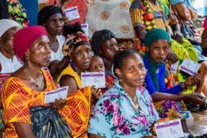 Group of women seated closely at a community event, each holding small identification or form cards.