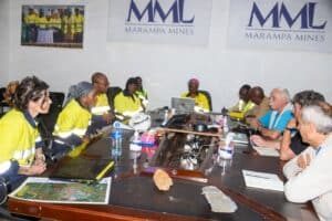 Team of workers in yellow safety vests seated around a conference table with laptops and papers; Marampa Mines banners on the wall.