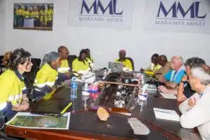 Team of workers in yellow safety vests seated around a conference table with laptops and papers; Marampa Mines banners on the wall.