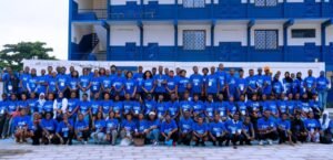 Large group of people wearing blue PMC shirts posing for a group photo in front of a blue and white building.