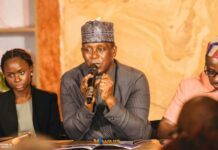 Dr. Kandeh Yumkella Launches WAIIS Media Campaign as Sierra Leone Prepares to Host Major West African Investment Summit Man in a patterned kufi hat speaks into a microphone at a panel discussion, flanked by a woman on his left and a man on his right.