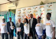 GERGHANSAL 2027 Unveiled in Freetown to Strengthen Cultural Ties Among Sierra Leone, Ghana and Germany Eight people pose for a photo at a promotional event, several in white logo T‑shirts and a few in suits, standing in front of a branded backdrop.