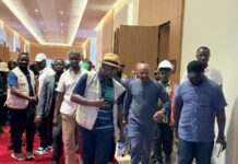 Vice President Inspects JMB International Conference Centre Ahead of WAIIS 2026 Diverse group walking down a hotel hallway on a red carpet, some wearing vests and hats.