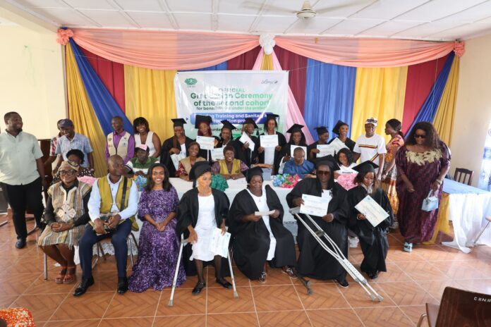 Group of graduates in caps and gowns holding certificates at a colorful ceremony backdrop in a hall.