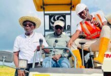 Rev. Pastor Francis Mambu Showcases 600-Acre Rice Harvest, Unveils 1,000 Bags for Sale Three workers sit on a yellow farming machine in a field; one wears a straw hat, one cap, and another a safety vest and hard hat.