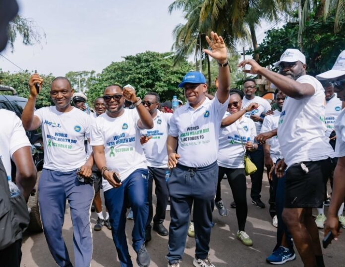 Diverse group of adults in white World Mental Health Day shirts marching together on a sunny street, raising hands in a celebratory pose.