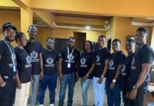 Highwoods Institute Expands Opportunities for Professional Accountancy Training and Digital Skills in Sierra Leone Eleven people in black T-shirts with white logos pose for a group photo indoors, wearing lanyards in a yellow-walled room.
