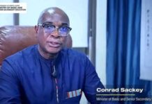 47,454 WASSCE Results Withheld as Alfred Farwell Thorpe Emerges Best Pupil & Awada Emerges Best-Performing School Conrad Sackey, Minister of Basic and Senior Secondary Education, seated in a blue shirt in an office, with the government of Sierra Leone logo in the top-left.