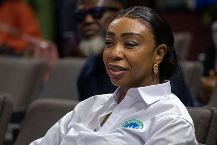 Woman with dark hair in a white button-down shirt, seated at an event, smiling slightly.